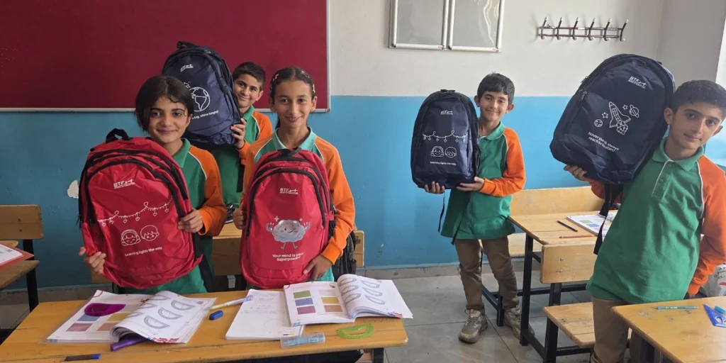 Five students at a school in Kars, Türkiye, smile while holding red and navy BTF backpacks provided through the Back to School Campaign.