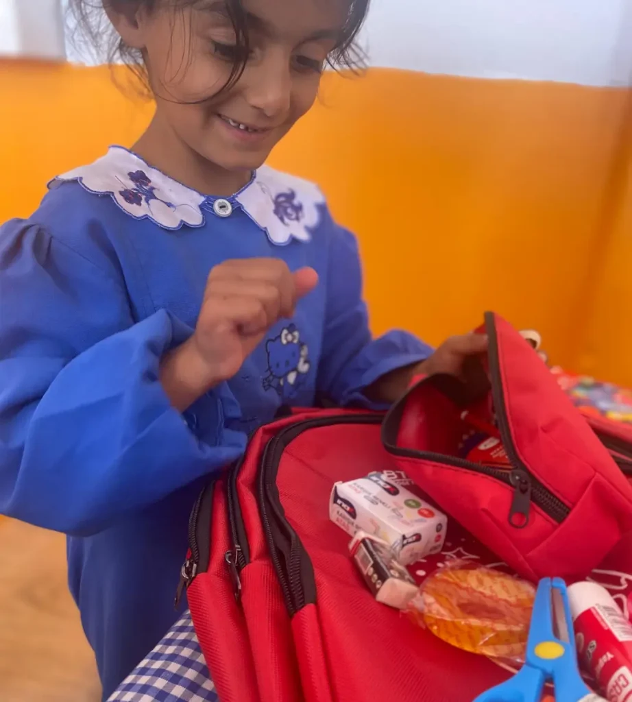 A student in a blue school uniform explores a new red backpack and pencil case filled with school supplies.