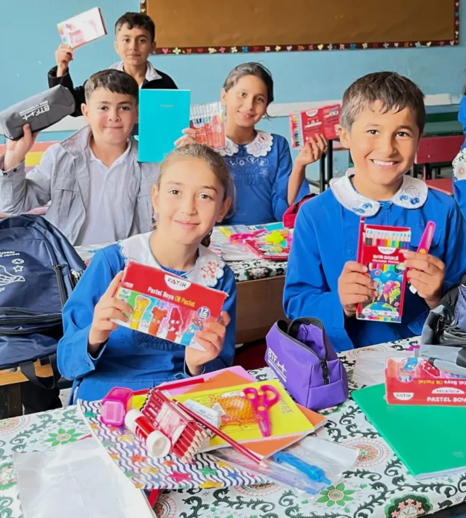 Five students at Azıklı Elementary School smile while displaying new notebooks, colored pencils, pastels, and pencil cases provided through BTF's Back to School Campaign.