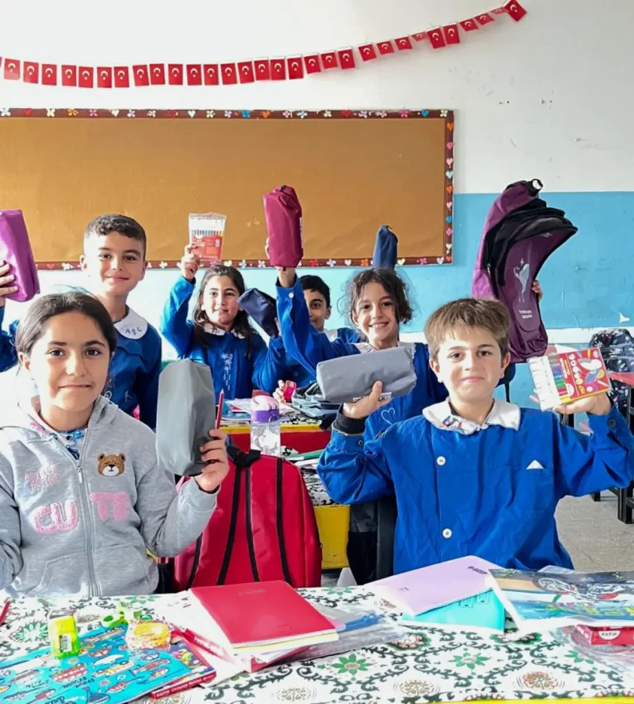 Students at Azıklı Elementary School in Şanlıurfa, Türkiye, hold up new pencil cases, colored pencils, and other school supplies in their classroom.