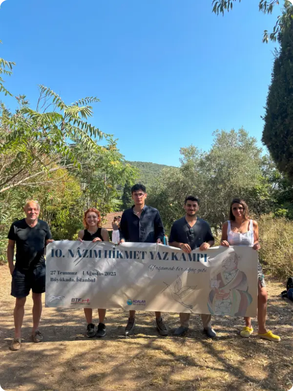 Five participants and organizers of the 2025 Nâzım Hikmet Summer Camp hold a camp banner outdoors in Büyükada, Istanbul.