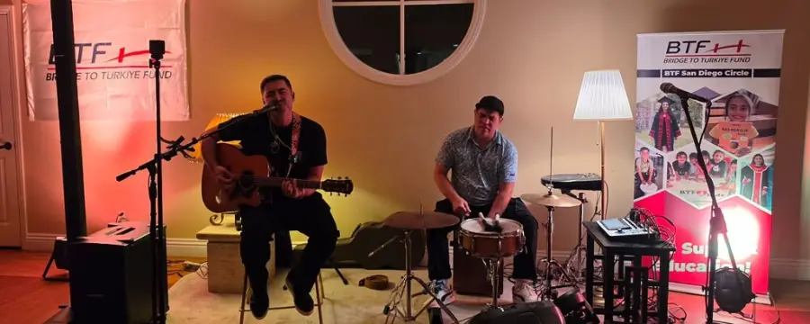 Two musicians perform live at Bridge to Türkiye Fund’s San Diego Giving Circle Third Wine Night, with one playing acoustic guitar and singing and the other playing drums.